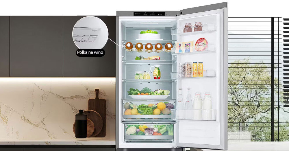Otwarta lodówka z widocznymi półkami wypełnionymi różnymi produktami spożywczymi, takimi jak warzywa, owoce, napoje i słoiki. Na obrazie znajduje się także powiększenie półki na wino z podpisem \'Półka na wino\'.