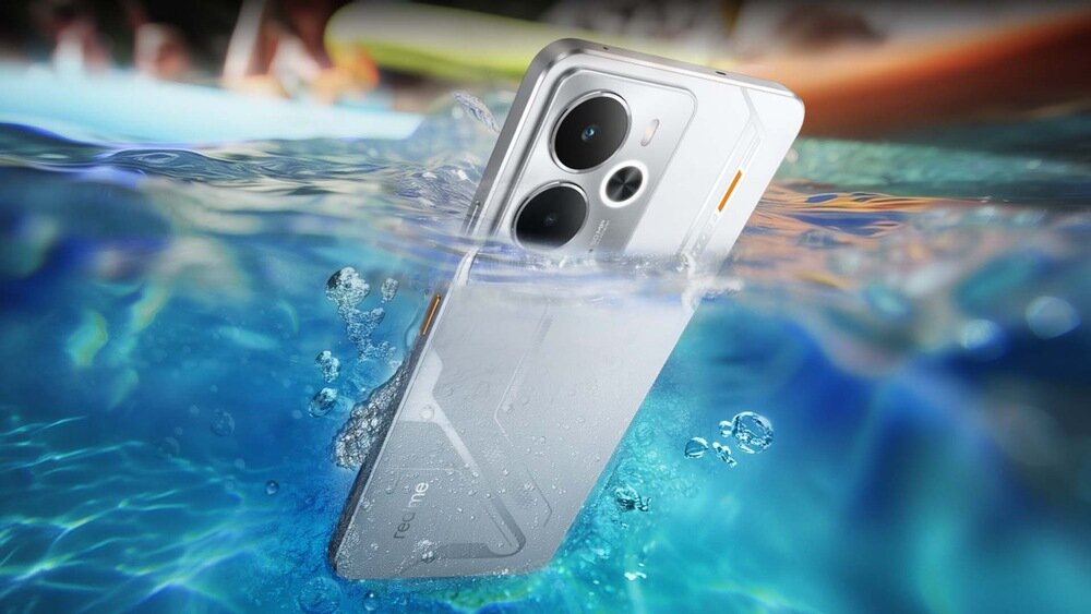 Srebrny smartfon zanurzony w wodzie, widoczny napis \'realme\' na obudowie. W tle rozmyty obraz basenu i ludzi.