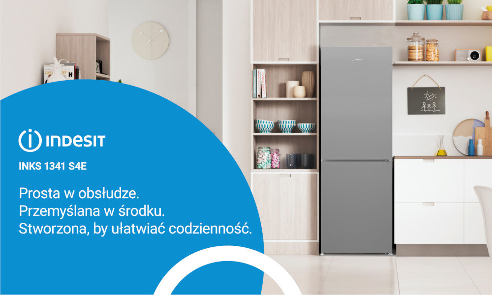 Obraz przedstawia kuchnię z lodówką w kolorze inox, obok której znajdują się półki z naczyniami i dekoracjami. Po lewej stronie widoczny jest niebieski panel z logo \'INDESIT INKS 1341 S4E\' oraz tekstem: \'Prosta w obsłudze. Przemyślana w środku. Stworzona, by ułatwiać codzienność.\'