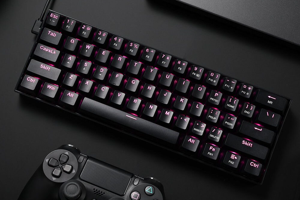 Na obrazie widoczna jest klawiatura mechaniczna z podświetleniem RGB, umieszczona na ciemnym tle. Obok klawiatury znajduje się kontroler do konsoli.