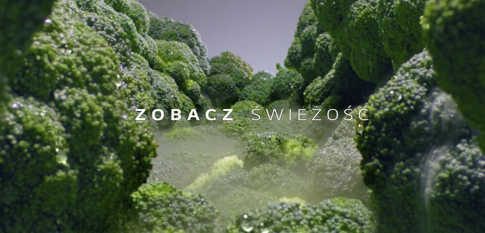 Obraz przedstawia zbliżenie na świeże brokuły pokryte kroplami wody. Na środku widoczny jest tekst: \'ZOBACZ ŚWIEŻOŚĆ\'.