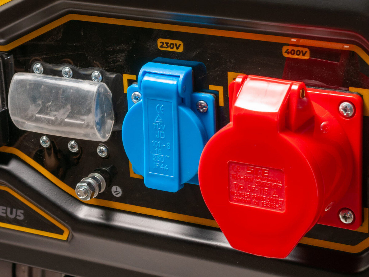 Obraz przedstawia panel z gniazdami elektrycznymi na agregacie prądotwórczym. Widoczne są niebieskie gniazdo oznaczone jako 230V i czerwone gniazdo oznaczone jako 400V.