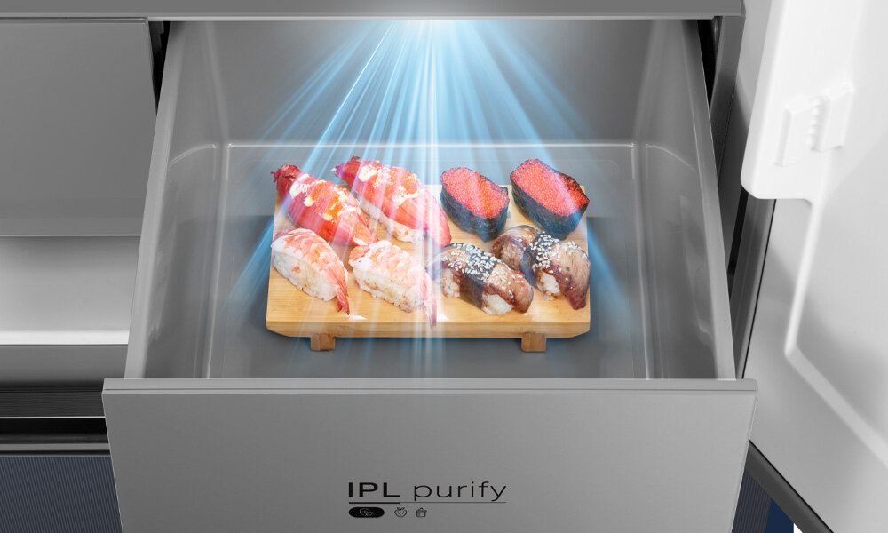 Wnętrze szuflady lodówki z drewnianą deską, na której znajduje się sushi, oświetlone niebieskim światłem. Na froncie szuflady widoczny jest napis \'IPL purify\'.