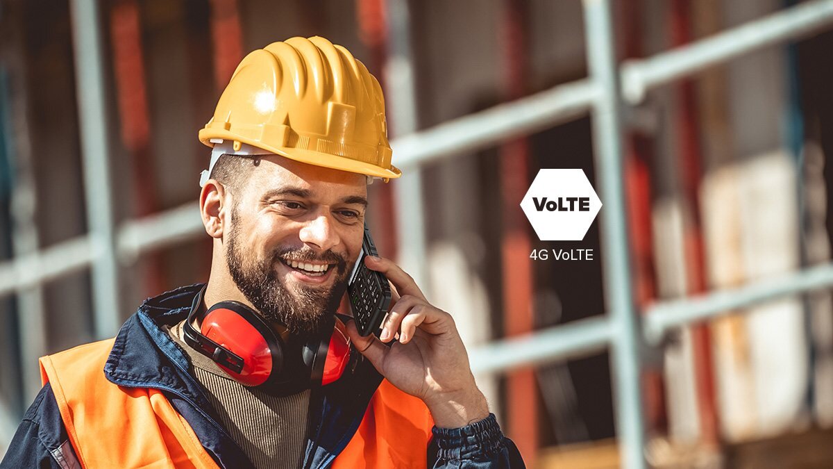 Mężczyzna w kasku ochronnym i kamizelce odblaskowej rozmawia przez telefon. Obok widoczny jest napis \'VoLTE 4G VoLTE\'.