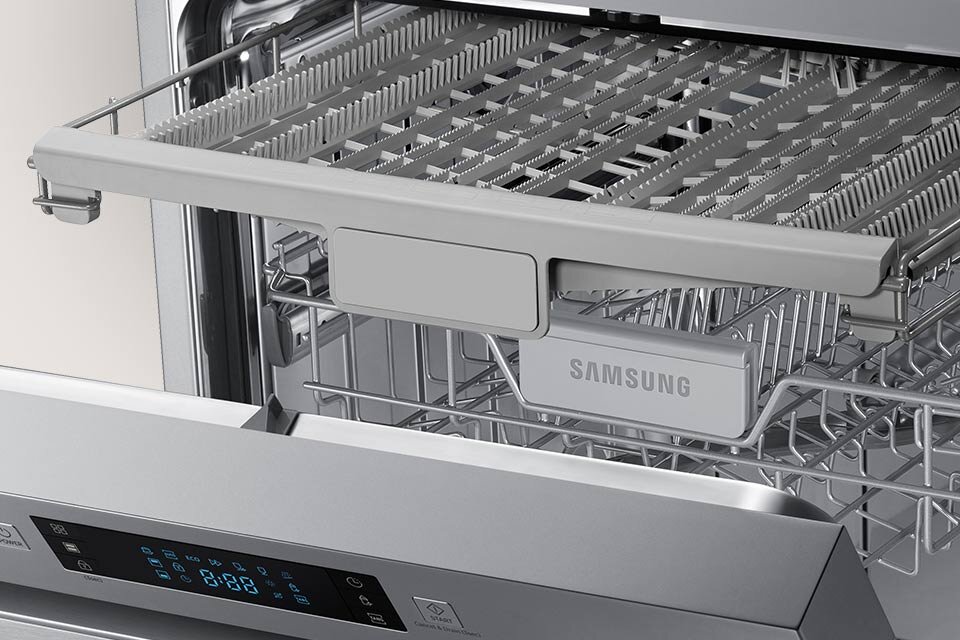 Wnętrze zmywarki z widocznym górnym koszem na sztućce i dolnym koszem na naczynia. Na jednym z elementów widoczny jest napis \'SAMSUNG\'.