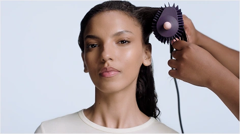 Ta sama modelka w ujęciu na wprost podczas modelowania włosów. Stylista nawija pasmo włosów na urządzenie Dyson Airsmooth.