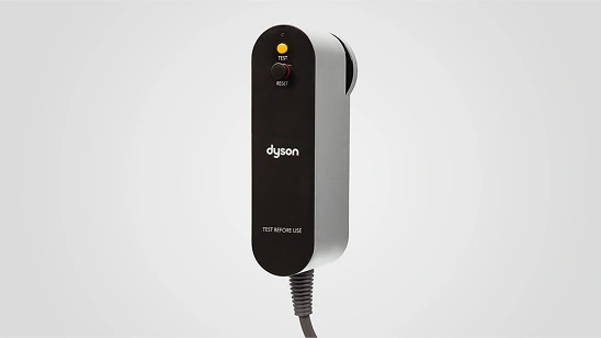 Urządzenie w kształcie prostokąta z zaokrąglonymi krawędziami, z widocznym logo \'dyson\' oraz przyciskami \'TEST\' i \'RESET\'. Na dole znajduje się napis \'TEST BEFORE USE\' oraz przewód zasilający.