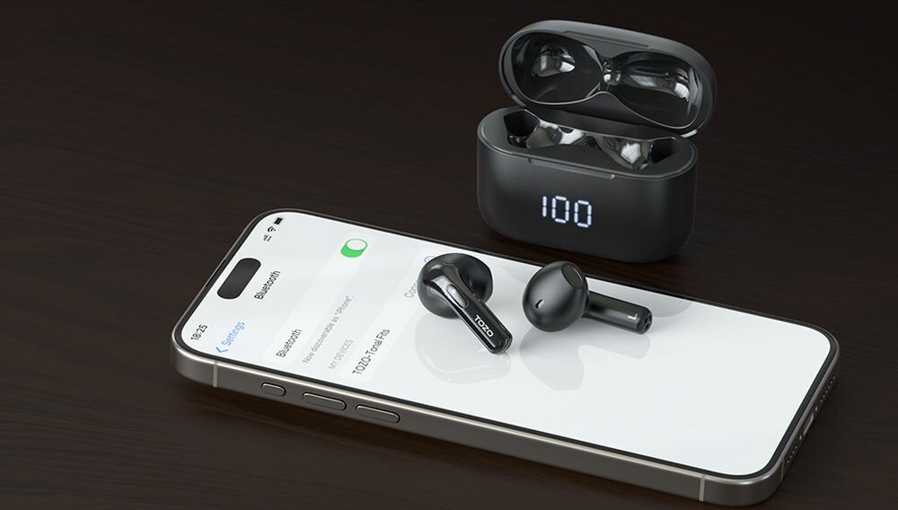 Na ciemnym tle leży smartfon z włączonym ekranem, na którym widoczna jest lista urządzeń Bluetooth, oraz czarne słuchawki douszne z napisem \'TOZO\'. Obok znajduje się otwarte etui ładujące z wyświetlaczem pokazującym liczbę \'100\'.