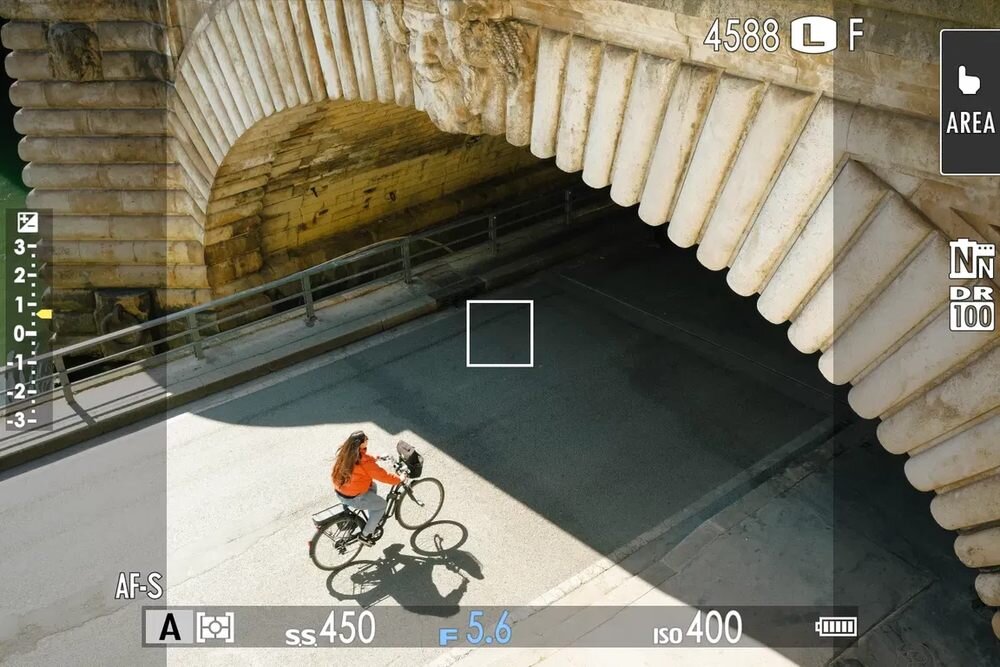 Zdjęcie przedstawia osobę na rowerze przejeżdżającą pod kamiennym mostem. Na obrazie widoczne są elementy interfejsu aparatu fotograficznego, takie jak ustawienia AF-S, ss 450, F 5.6, ISO 400.
