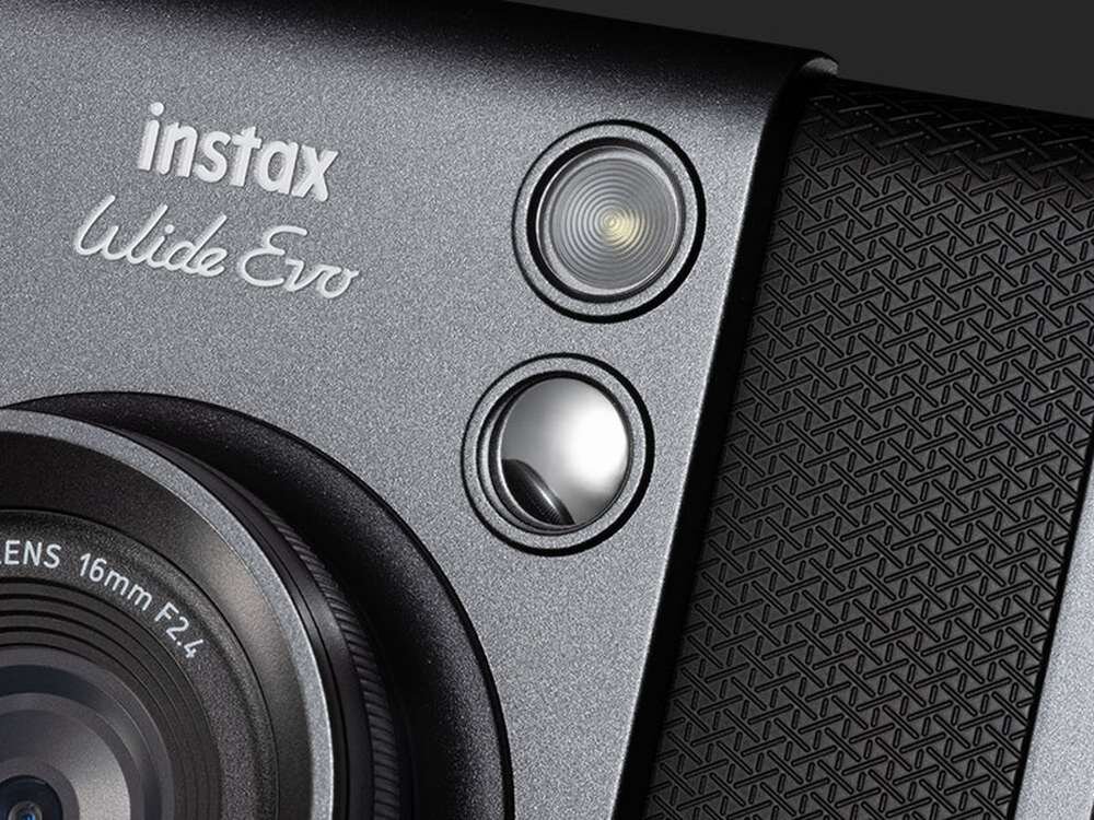 Zbliżenie na aparat fotograficzny z widocznym obiektywem i dwoma przyciskami. Na obudowie widoczny jest napis \'instax Wide Evo\'.