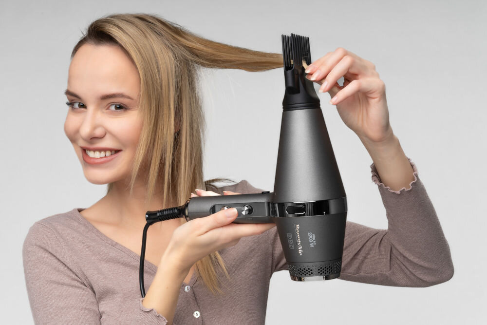 Osoba używa suszarki do włosów BEAUTYME Keratin Intense HD925 2200W, trzymając pasmo włosów. Suszarka jest koloru ciemnego z widocznym logo i napisem \'Keratin Intense\'.