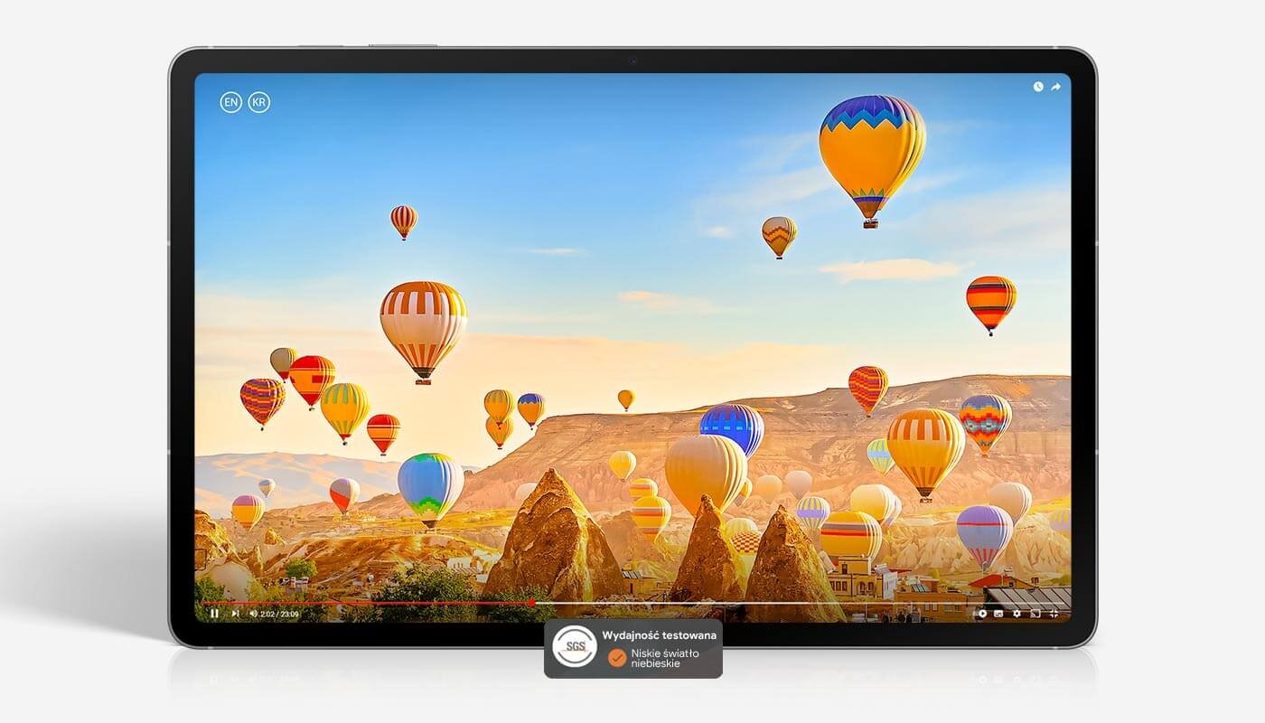 Na ekranie serii Galaxy Tab S10 FE odtwarzany jest film przedstawiający kolorowe balony na ogrzane powietrze lecące nad pustynnym krajobrazem, prezentujący jasny, żywy obraz na wyświetlaczu. Pokazano logo SGS Performance Tested Low Blue-light Ex. Tablet wyświetla kolorowy obraz z balonami unoszącymi się nad skalistym krajobrazem. Na ekranie widoczny jest tekst: \'Wydajność testowana\' oraz \'Niebo i światło niebieskie\'.