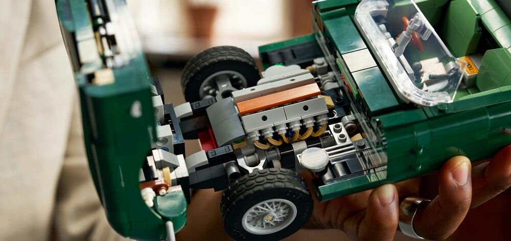 Osoba trzyma model samochodu z klocków LEGO, przedstawiający zielony pojazd z widocznym silnikiem i szczegółami konstrukcji. Wnętrze samochodu jest częściowo widoczne przez przezroczystą szybę.