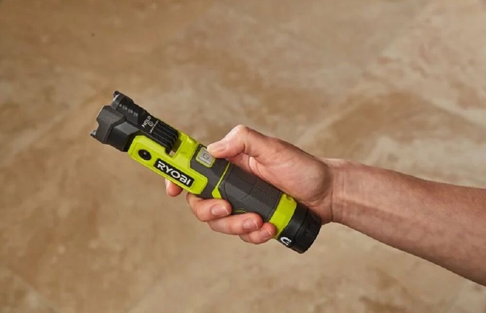 Latarka RYOBI USB Lithium RLP4-0, latarka, laser, mobilność, warsztat, Dłoń trzymająca i włączająca latarkę akumulatorową.