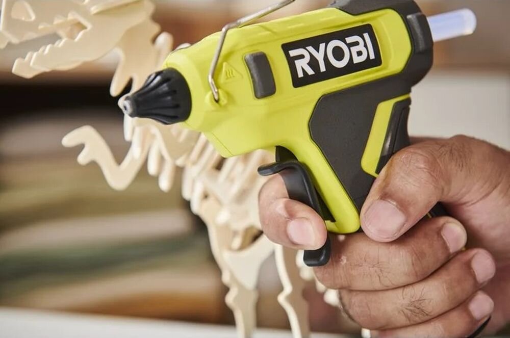 Pistolet do kleju RYOBI RGLU4-0, lithium, akumulator, czas, wydajność, Dłoń trzymająca pistolet na klej przy makiecie.