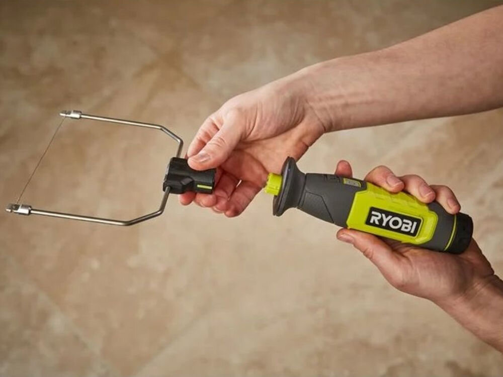 Osoba trzyma narzędzie z logo \'RYOBI\', które ma metalową ramę z cienkim drutem. Tło jest jednolite, w jasnym kolorze.