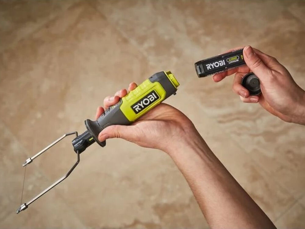 Osoba trzyma nóż termiczny z widocznym logo \'RYOBI\' oraz akumulator z napisem \'RYOBI Lithium 4V\'.