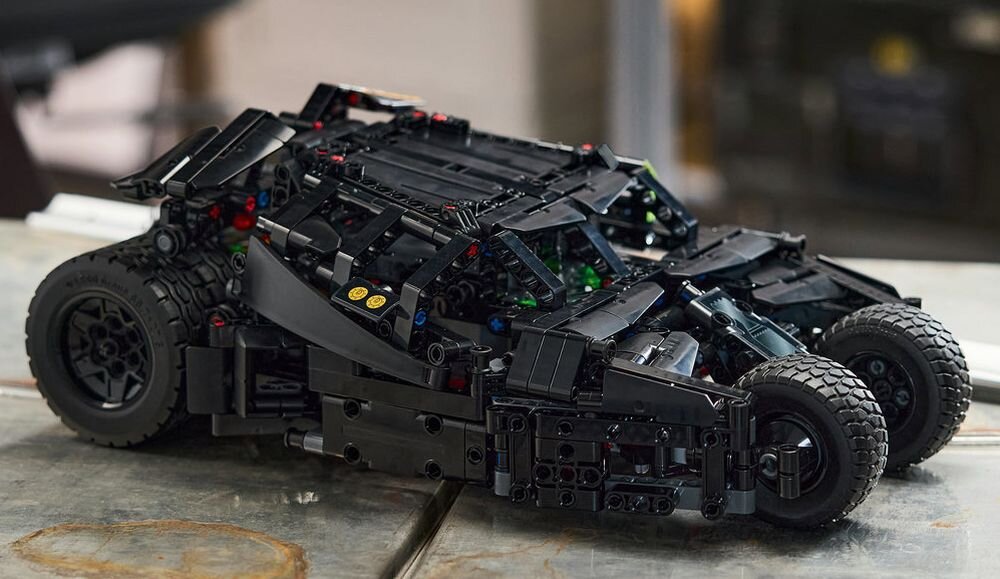 Model samochodu z klocków LEGO w kolorze czarnym, z widocznymi szczegółami konstrukcji i dużymi kołami, ustawiony na powierzchni przypominającej metalowy stół.
