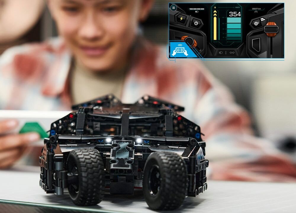 Na pierwszym planie znajduje się model LEGO pojazdu z dużymi kołami, a w tle osoba trzymająca urządzenie. W prawym górnym rogu widoczny jest interfejs z liczbą \'354\' i różnymi wskaźnikami.