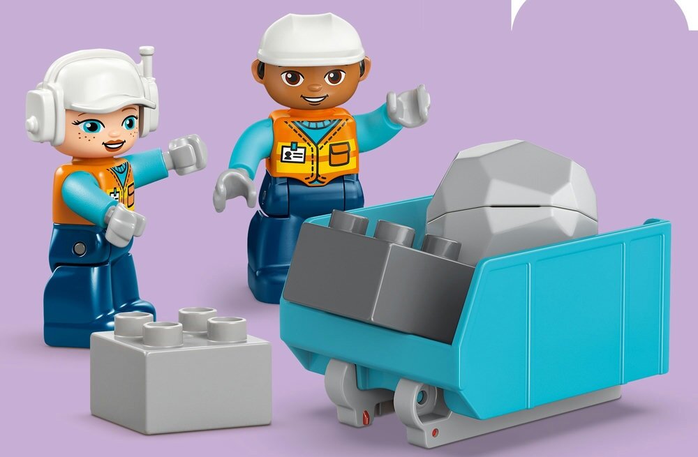 Na fioletowym tle znajdują się dwie figurki LEGO w kaskach i kamizelkach oraz niebieska wywrotka z szarym kamieniem. Obok leży szary klocek LEGO.