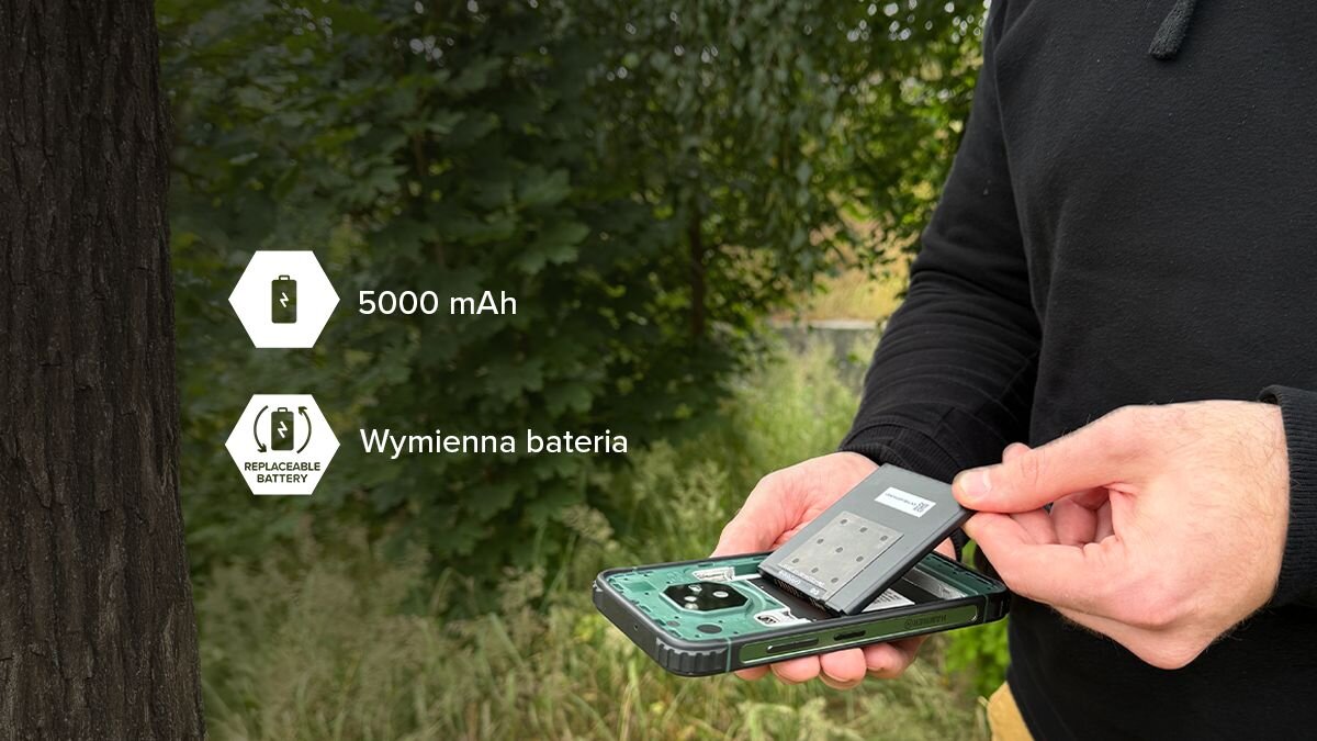 Osoba trzyma smartfon z wyjętą baterią na tle drzew. Na obrazie widoczny jest tekst: \'5000 mAh\' oraz \'Wymienna bateria\'.
