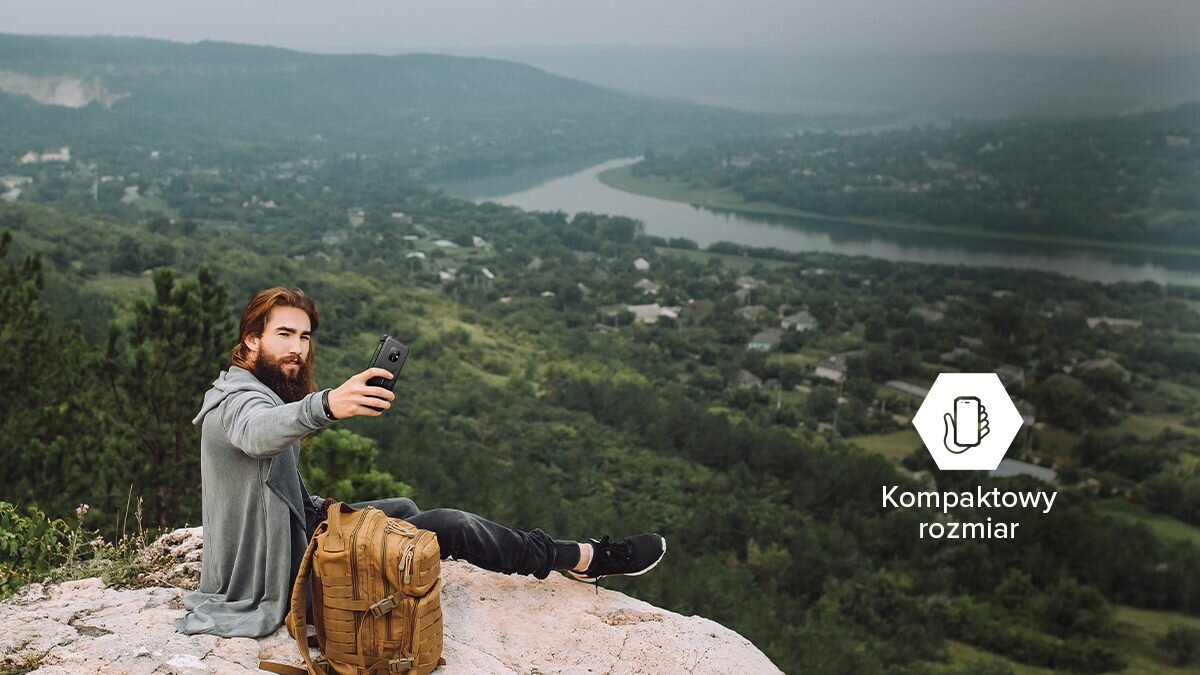 Osoba siedzi na skale z plecakiem, trzymając smartfon, w tle widoczny jest krajobraz z rzeką i lasem. Obok znajduje się ikona z napisem \'Kompaktowy rozmiar\'.