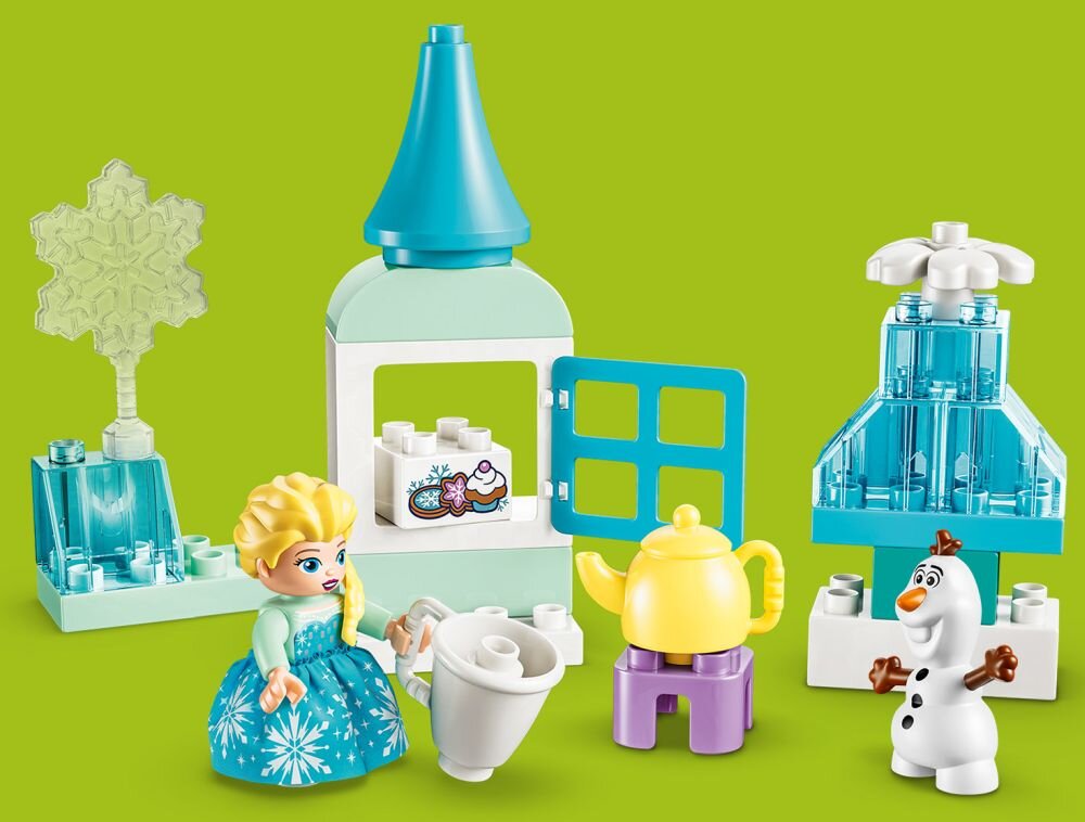 Zestaw klocków LEGO przedstawia postacie i elementy z Krainy Lodu, w tym figurki Elzy i Olafa oraz różne akcesoria, takie jak dzbanek i filiżanka. W tle widoczne są konstrukcje z klocków w kolorach niebieskim i białym na zielonym tle.