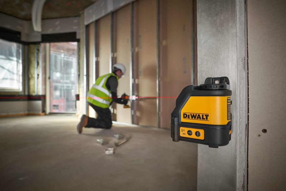 Laser krzyżowy DEWALT DW088K, laser, miara, wiązka, budowa, laser zamontowany do ściany, w tle robotnik pracujący na budowie