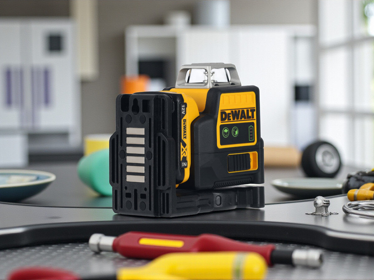 Laser liniowy DEWALT DCE0811D1G-QW, 12 godzin, impulsowe, detektor, wahadło, na metalowej powierzchni, w tle rozmyty użytkownik podczas pracy oraz elementy wyposażenia biurowego