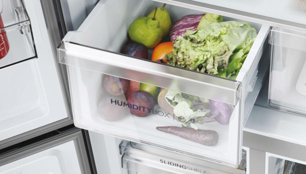 Widoczna jest szuflada lodówki z napisem \'HUMIDITY BOX\', wypełniona różnymi owocami i warzywami, takimi jak sałata, gruszka, śliwki i marchewka.
