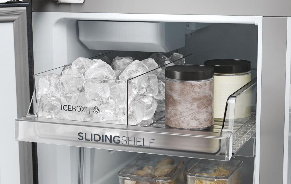 Wnętrze lodówki z wysuwaną półką oznaczoną jako \'SLIDINGSHELF\', na której znajduje się pojemnik z lodem z napisem \'ICEBOX\' oraz dwa pojemniki z czarnymi pokrywkami.