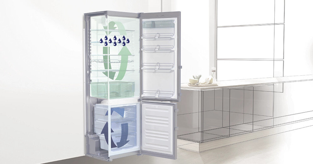 Otwarta lodówka z widocznymi półkami i szufladami, na których znajdują się symbole strzałek i kropli wody. W tle widać jasną kuchnię z blatem i oknem.