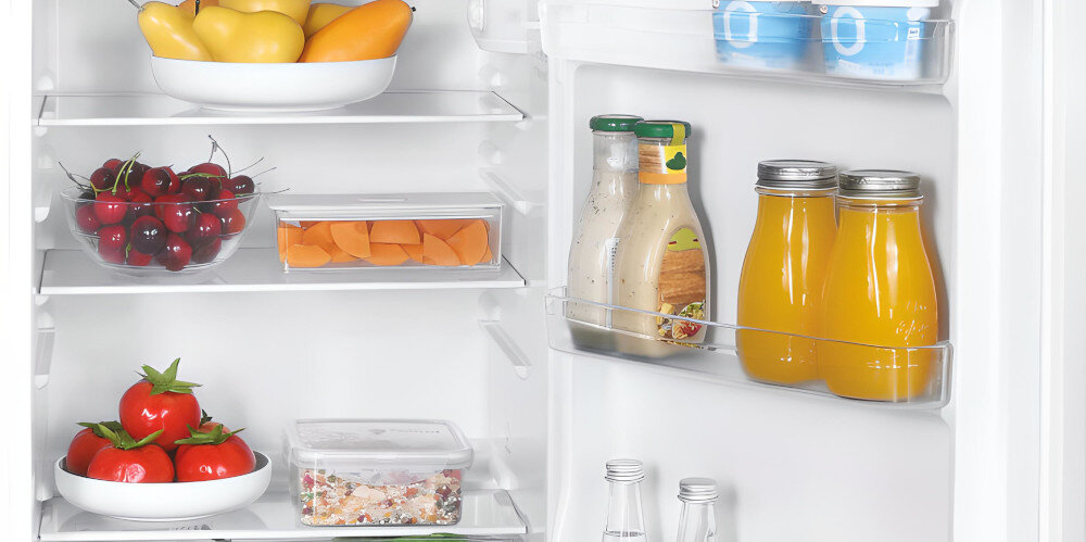Wnętrze lodówki z półkami wypełnionymi różnymi produktami spożywczymi, takimi jak owoce, warzywa, napoje i sosy. Na drzwiach lodówki znajdują się butelki z sokiem i sosami.