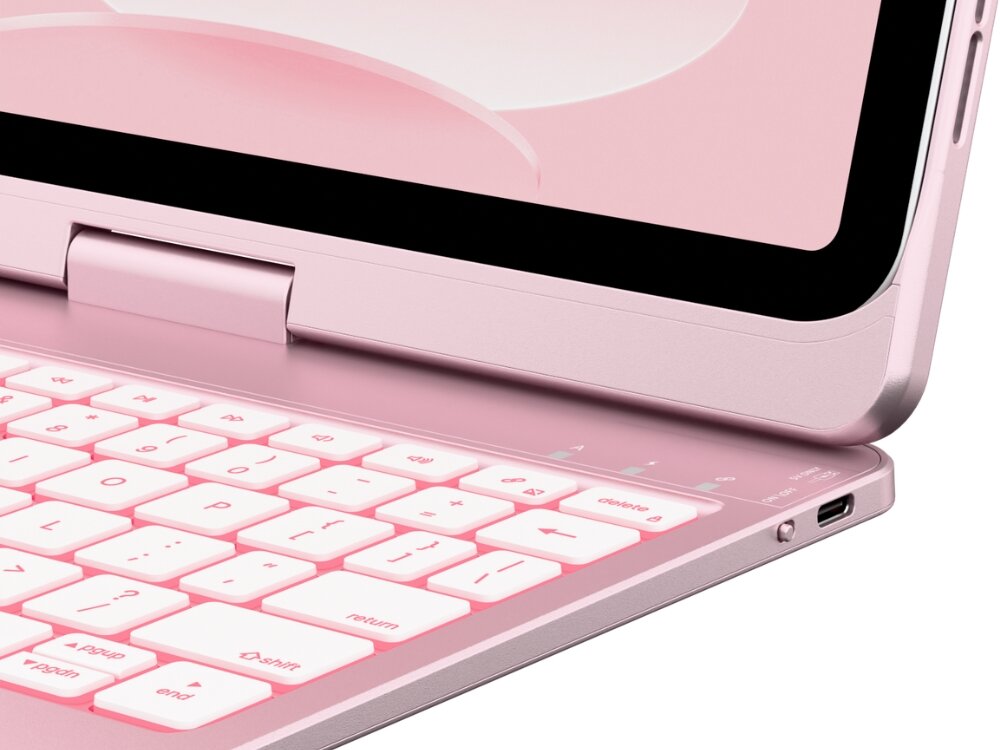 Jasnoróżowe etui na iPad z klawiaturą, z widocznymi klawiszami i portem USB. Klawiatura ma podświetlane klawisze z oznaczeniami, takimi jak \'return\' i \'delete\'.