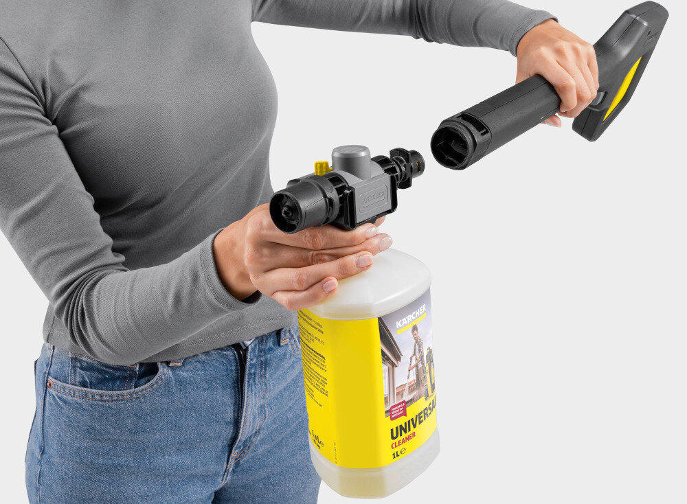 Osoba trzyma butelkę z żółtą etykietą z napisem \'UNIVERSAL CLEANER\' oraz czarną dyszę myjki ciśnieniowej. Na etykiecie widoczne jest logo \'KARCHER\'.