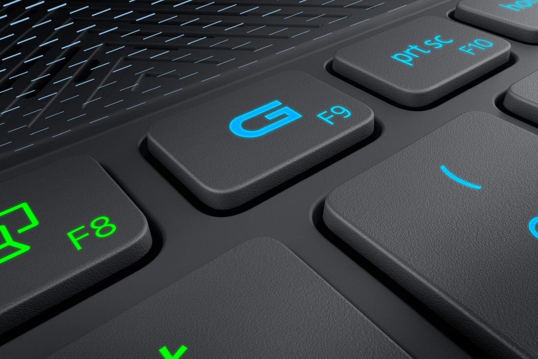 Zbliżenie na klawiaturę laptopa z widocznymi klawiszami: F8 z zieloną ikoną, G F9 w kolorze niebieskim, oraz prt sc F10. Tło klawiatury ma wzór geometryczny.