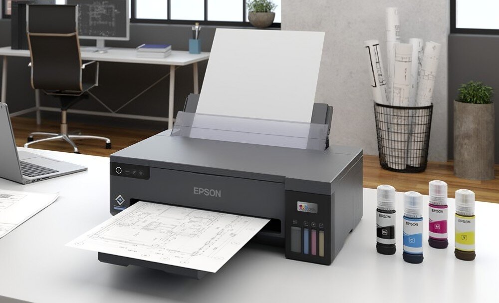 Na biurku znajduje się drukarka z logo EPSON, z której wychodzi zadrukowana kartka. Obok drukarki stoją cztery butelki z tuszem w różnych kolorach.