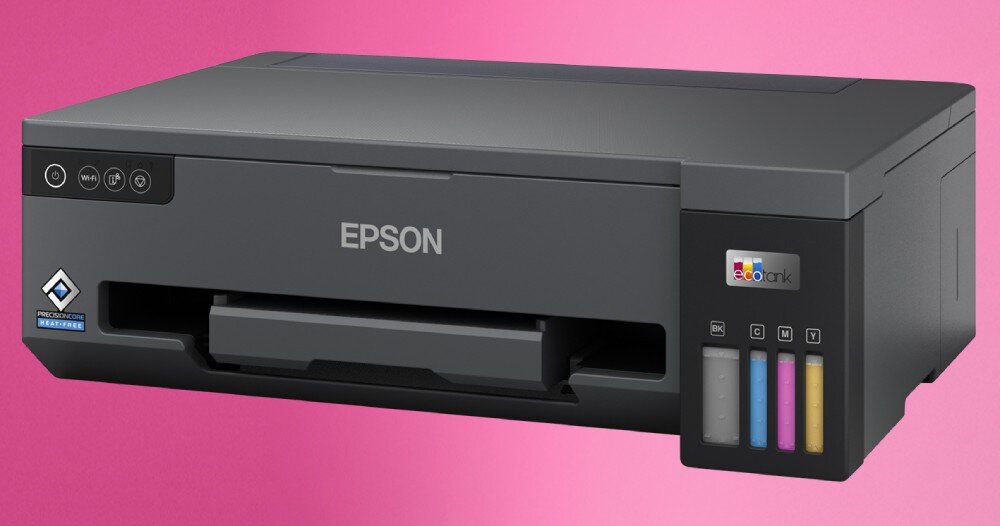 Na różowym tle znajduje się drukarka marki EPSON z widocznymi przyciskami na panelu oraz wskaźnikami poziomu tuszu w różnych kolorach. Na obudowie widoczne jest logo \'EcoTank\' oraz symbol \'Recommended Hardware\'.