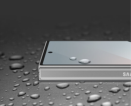 Smartfon leży na powierzchni pokrytej kroplami wody. Na krawędzi urządzenia widoczne jest częściowo logo \'SAMSUNG\'.
