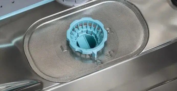 Wnętrze zmywarki z widocznym filtrem w kolorze niebieskim umieszczonym na metalowej siatce.