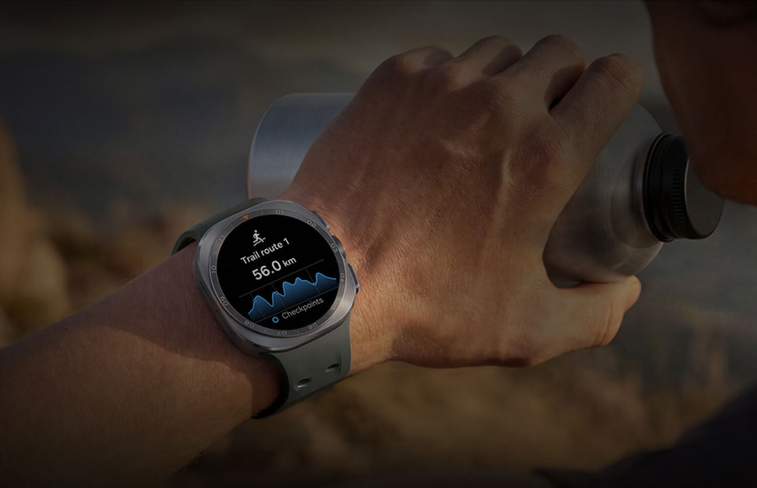 W terenie. Na dobrej drodze Osoba trzymająca metalowy bidon ma na nadgarstku smartwatch z wyświetlaczem pokazującym trasę o długości 56.0 km. Na ekranie widoczny jest wykres oraz napis \'0 Checkpoints\'.