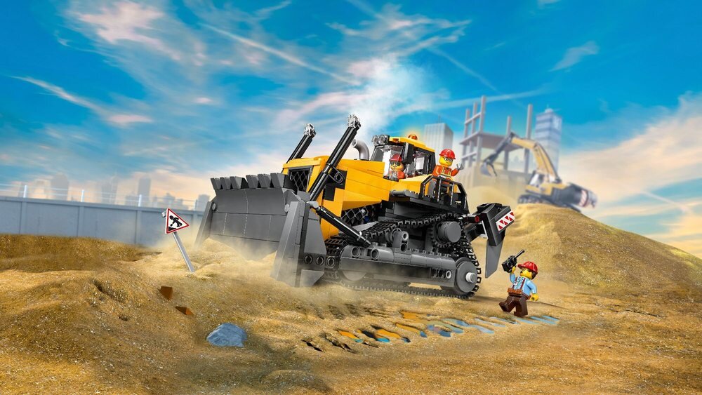 Na obrazie widać żółty buldożer LEGO na placu budowy, z dwoma figurkami pracowników w kaskach. W tle znajduje się niebieskie niebo i zarys miasta.