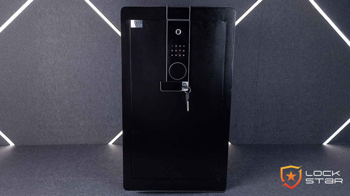 Czarny sejf z elektronicznym panelem na kod i odcisk palca, z kluczem w zamku. W prawym dolnym rogu widoczne jest logo \'LOCK STAR\'.