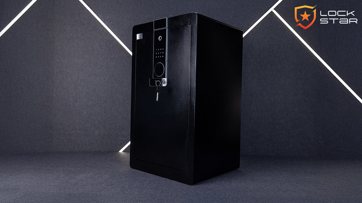 Czarny sejf z elektronicznym panelem na kod i odcisk palca, z widocznym kluczem w zamku. W prawym górnym rogu znajduje się logo z napisem \'LOCK STAR\'.