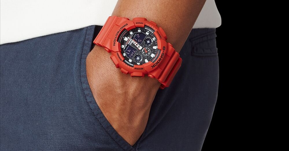 Osoba nosi czerwony zegarek sportowy na nadgarstku, z widocznym logo CASIO na tarczy. Zegarek ma cyfrowy i analogowy wyświetlacz oraz masywną obudowę.