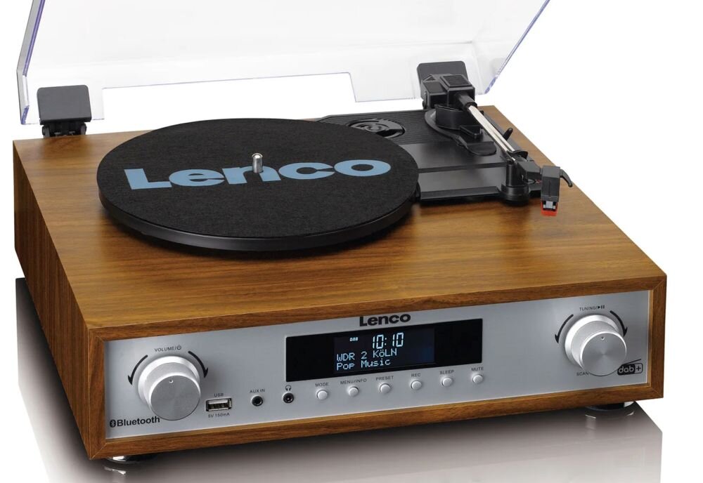 Gramofon z drewnianą obudową i przezroczystą pokrywą, na której widnieje logo \'Lenco\'. Na panelu przednim znajdują się pokrętła, wyświetlacz z napisem \'WDR 2 KÖLN Pop Music\' oraz kilka przycisków.