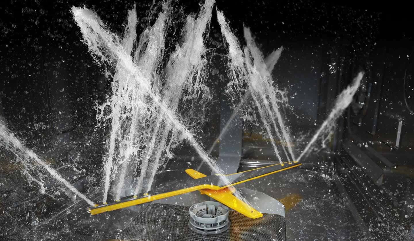 Najnowsza technologia Jet Clean Obraz przedstawia wnętrze zmywarki z widocznymi strumieniami wody tryskającymi z ramion spryskiwacza. Ramiona są koloru żółtego, a woda rozpryskuje się w różnych kierunkach.