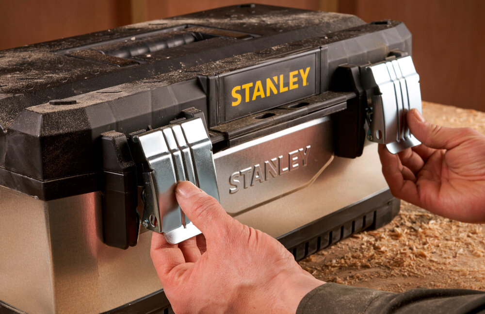 Skrzynka narzędziowa STANLEY 1-95-618 zbliżenie na zamki osoba otwiera skrzynię dwa solidne metalowe zamki bezpieczne przechowywanie narzędzi i akcesoriów ochrona zawartość przed przypadkowym otwarciem trwałość