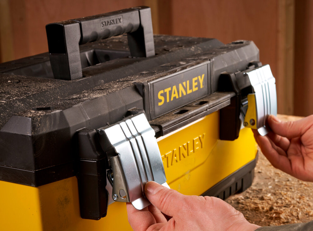 Skrzynka narzędziowa STANLEY Żółta 1-95-613 zbliżenie na zamki osoba otwiera skrzynię dwa solidne metalowe zamki bezpieczne przechowywanie narzędzi i akcesoriów ochrona zawartość przed przypadkowym otwarciem trwałość