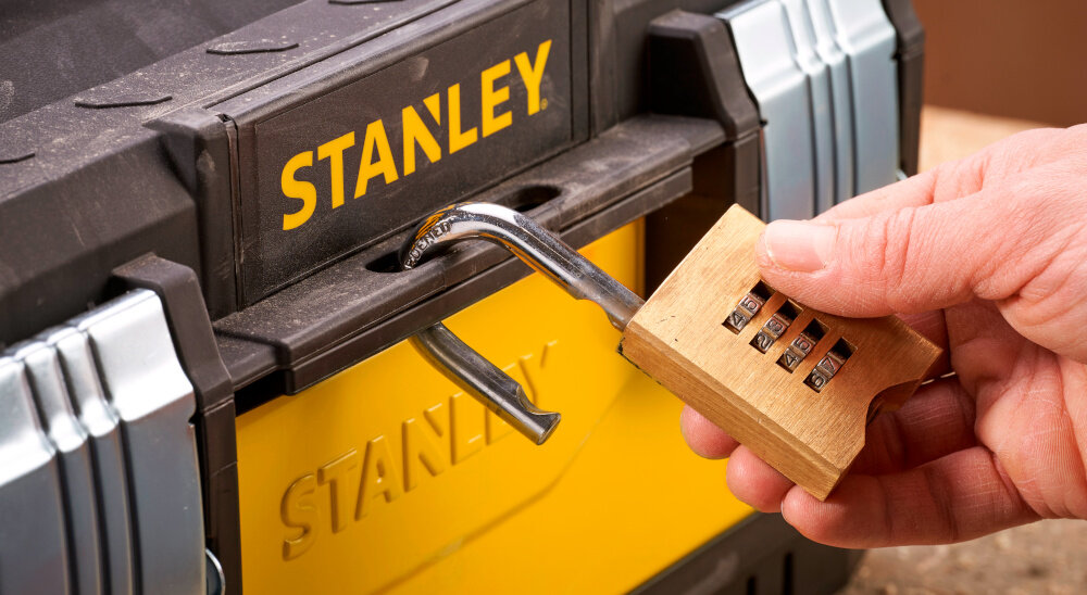 Skrzynia narzędziowa STANLEY 1-95-613 zbliżenie na otwór do kłódki osoba zakłada kłódkę na skrzynię otwór umożliwiający założenie kłódki bezpieczeństwo przechowywanych narzędzi